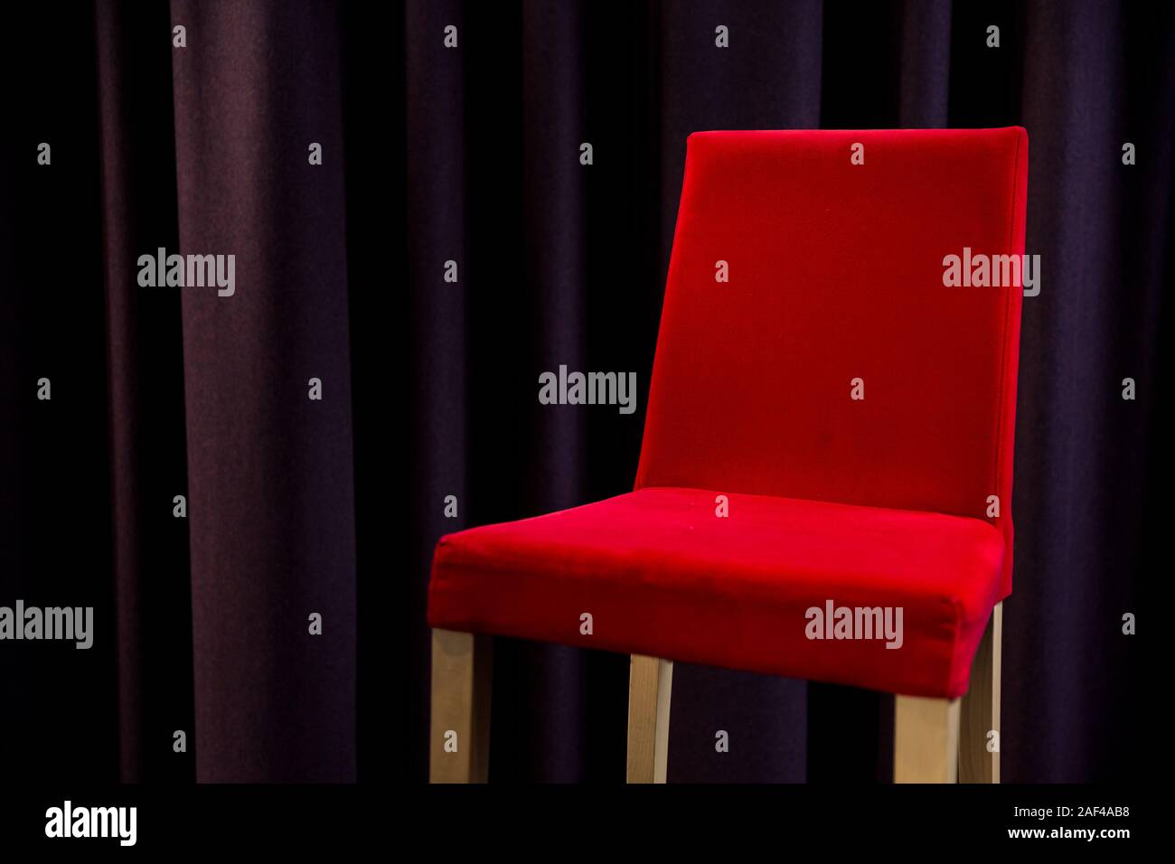 Ein roter Polsterstuhl neben lila Vorhänge. Stockfoto