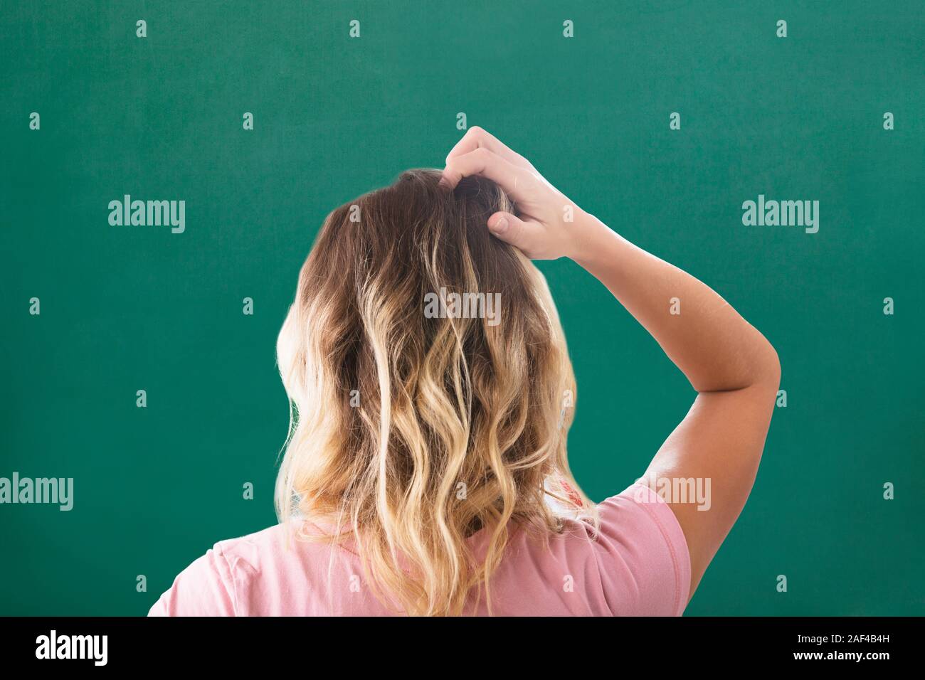 Ansicht der Rückseite des blonden Jungen Frau Kratzen ihren Kopf gegen Grüner Hintergrund Stockfoto