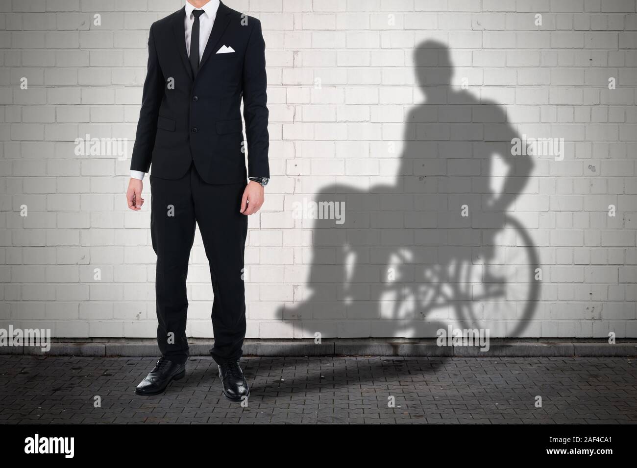 Unternehmer stehen gegen weiße Mauer mit Schatten eines Deaktivieren Mann sitzt auf Rollstuhl Stockfoto