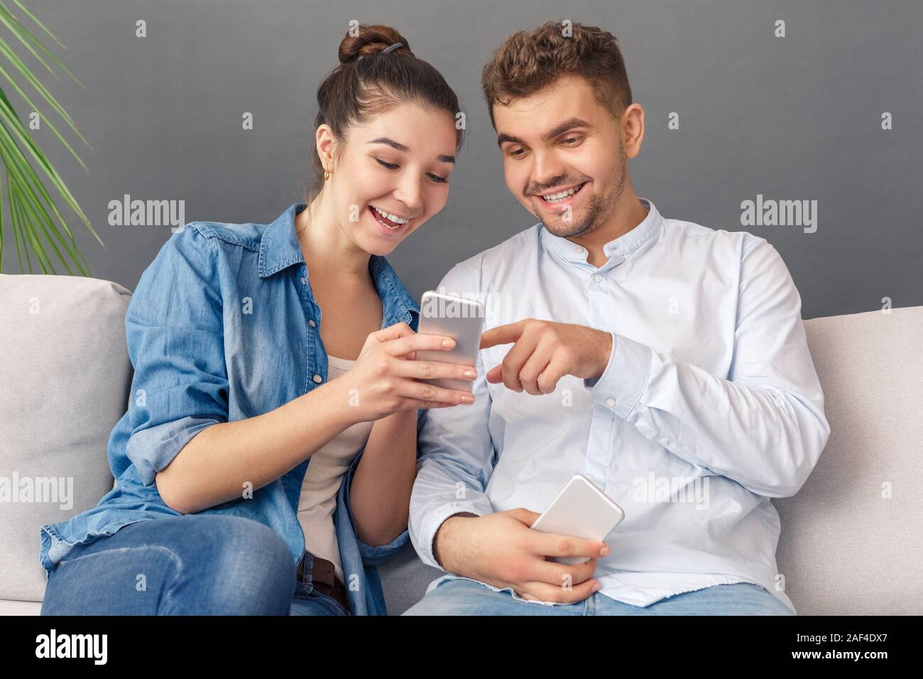 Relationnship Konzept. Junges Paar sitzt auf einem Sofa Studio auf grau Video isoliert auf dem Smartphone zusammen Lächeln aufgeregt Stockfoto