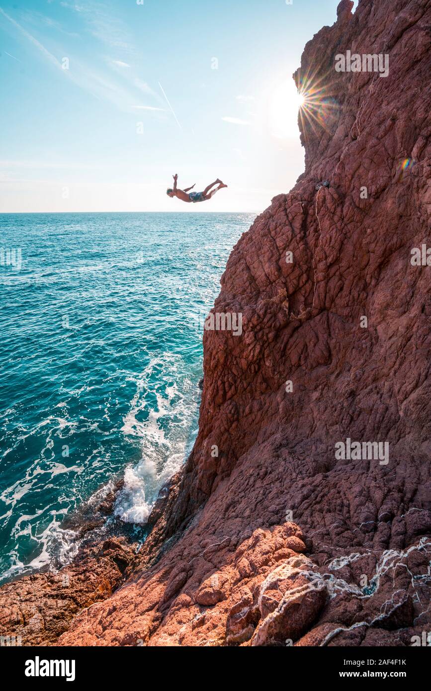 Junge männliche springt von rot sand Stone Cliff in Blue Ocean Stockfoto