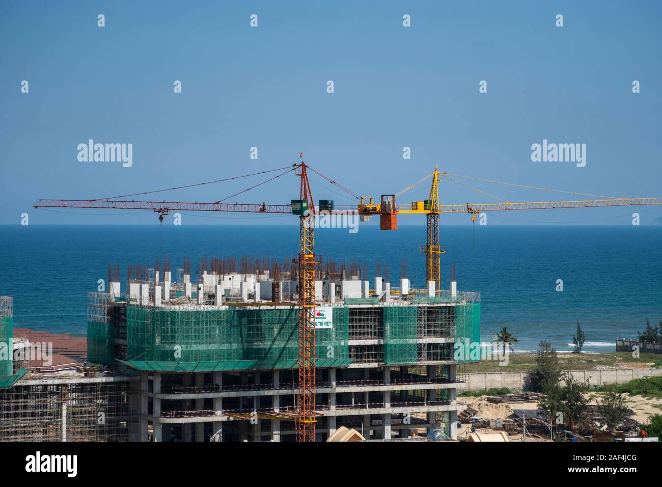 VIETNAM da NANG - April 10, 2019: Krane und Gebäude Baustelle gegen den blauen Himmel und das Meer. Metall Bau der unvollendete Gebäude auf Stockfoto