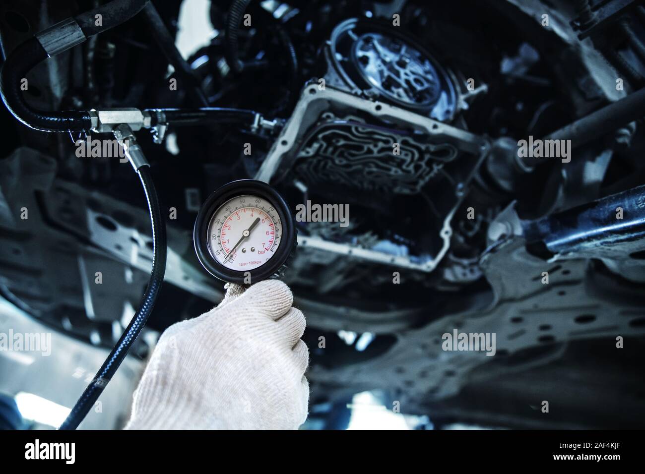 Hand in einem weißen Handschuh hält ein Manometer vor dem Hintergrund einer teilweise zerlegt Automatikgetriebe mit geringer Tiefenschärfe Stockfoto
