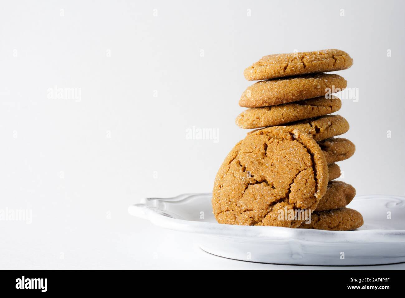 Eine ginger Cookie lehnt sich gegen einen Stapel von Ingwer Cookies auf einer weißen Platte und einen weißen Hintergrund mit Kopie Raum auf der linken Seite Stockfoto