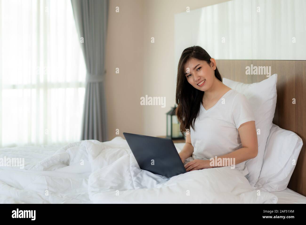 Portrait von schöne asiatische Frau entspannen mit Laptop und Kamera im Schlafzimmer. Lächeln glücklich asiatischen Mädchen online shopping zu Hause Bildung e-Commerc Stockfoto