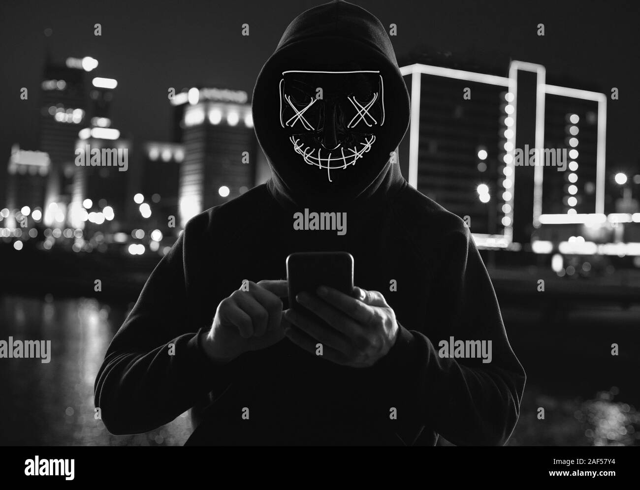 Porträt eines anonymen Mann in einem schwarzen Kapuzenpullover und Neon mask Hacker in ein Smartphone. Helle Stadt Hintergrund Stockfoto