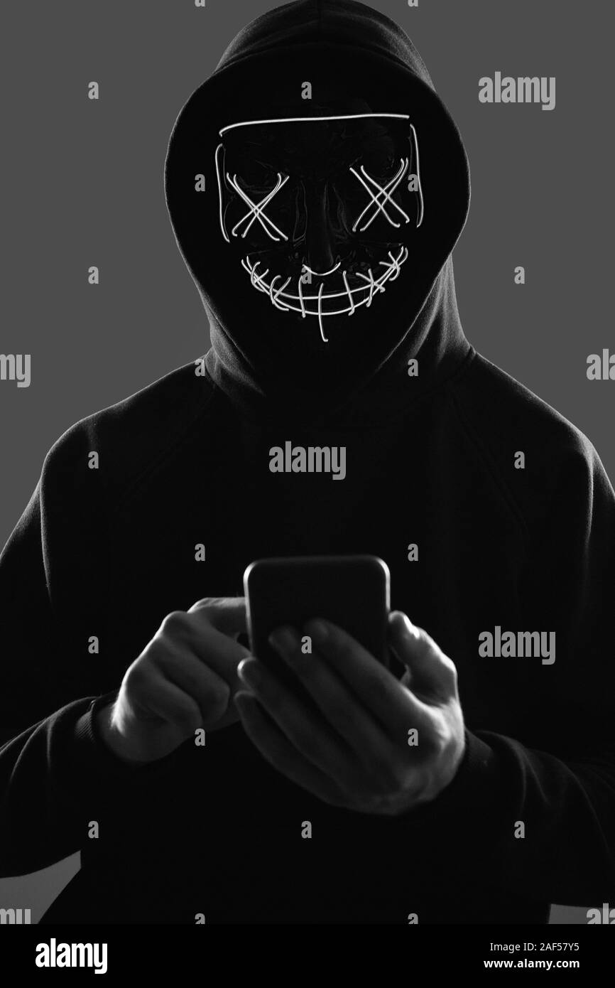 Porträt eines anonymen Mann in einem schwarzen Kapuzenpullover und Neon mask Hacker in ein Smartphone. Studio gedreht. Stockfoto