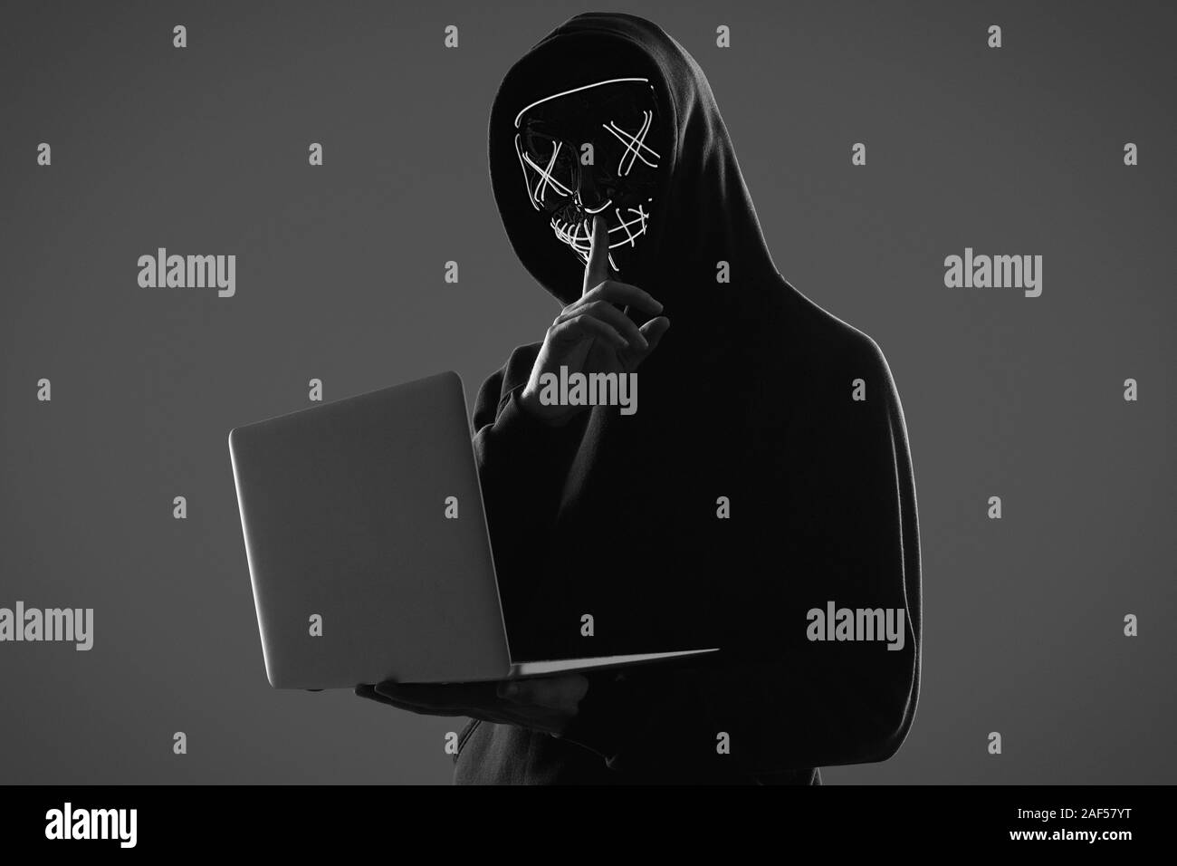 Porträt eines anonymen Mann in einem schwarzen Kapuzenpullover und Neon mask Hacking in einen Computer ein. Studio gedreht. Stockfoto