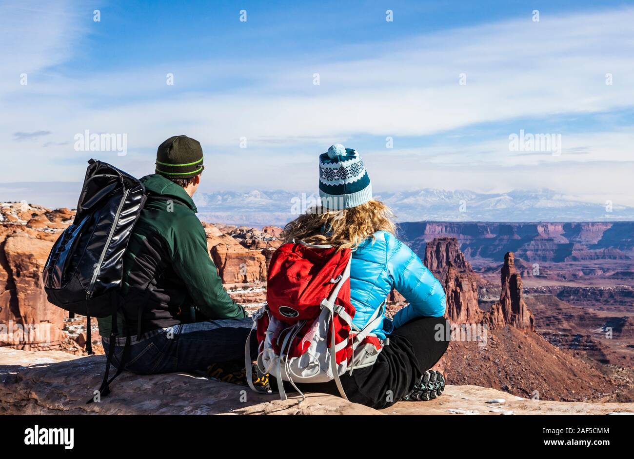 Ein Mann und eine Frau sitzen auf dem Rand des Canyon Wand den Blick über die schöne Landschaft des Canyonlands National Park und die La Sal Mountains, U Stockfoto