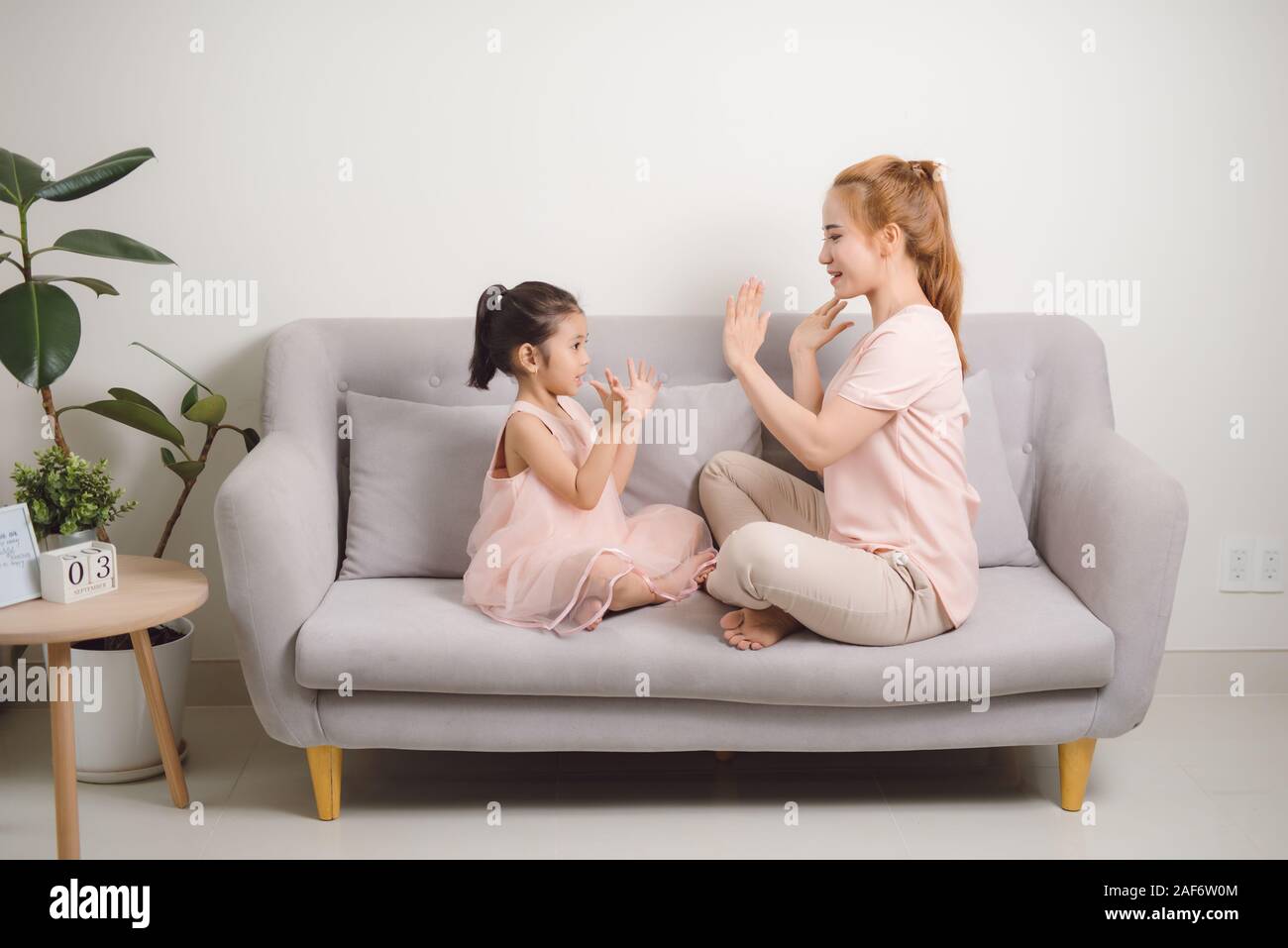 Glückliche junge Frau spielen klatschen Spiel mit weiblichen Kind, während im Wohnzimmer sitzen Stockfoto