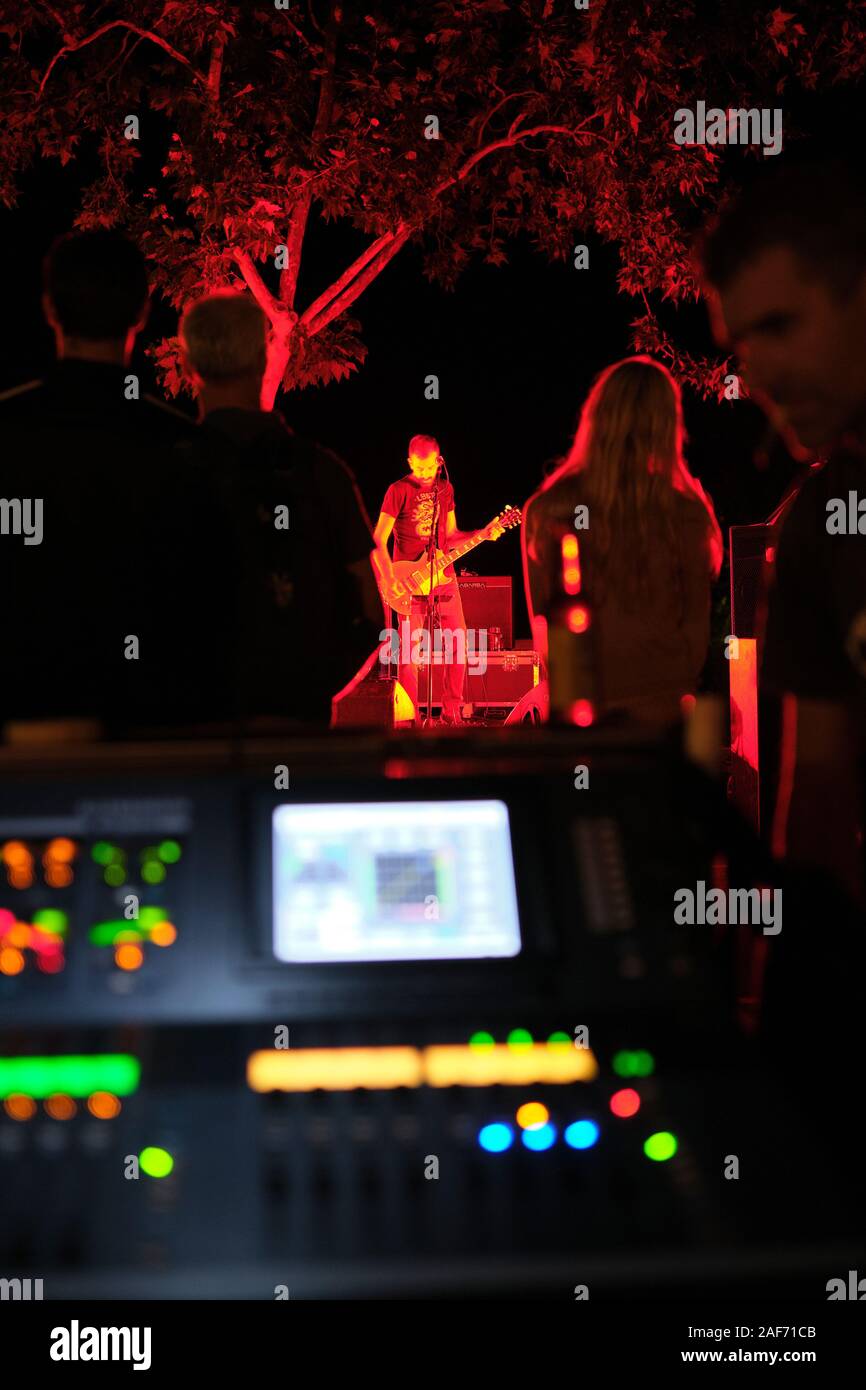 Einen kleinen outdoor abends Live Musik Bühne mit einer Band spielen und ein unscharf Vordergrund Sound Mixing Desk Console mit Beleuchtung. Stockfoto