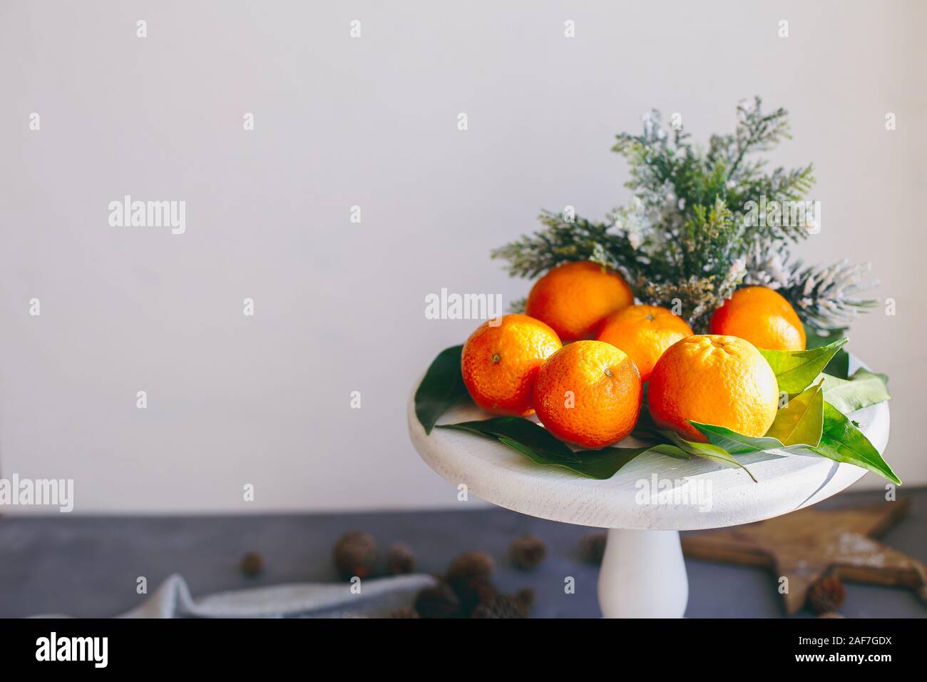 Orange Mandarinen auf grauem Hintergrund im Neuen Jahr Einrichtung mit braunen Tannenzapfen und grünen Blättern. Köstlich süßen Clementine. Weihnachtsdekoration mit Stockfoto