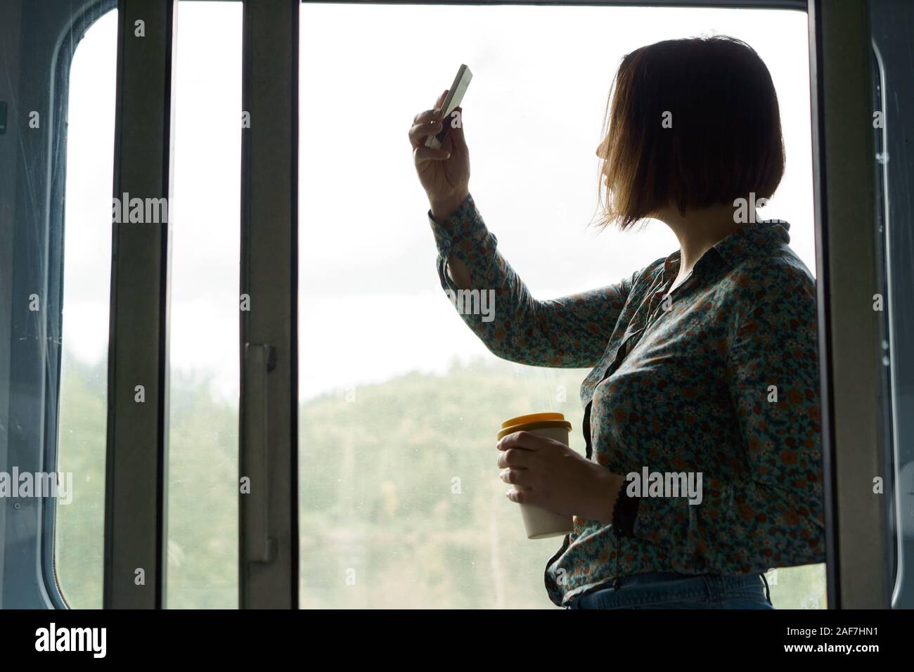 Hübsche Frau mit einem Telefon und einer Tasse Kaffee steht in der Bahn Stockfoto