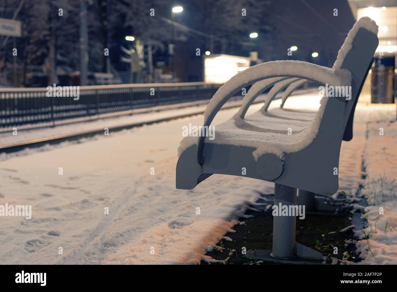 Freie Bank mit Schnee an einem leeren Bahnhof abgedeckt in der Nacht. Erwartung, Einsamkeit und Mobilitätskonzepte Stockfoto