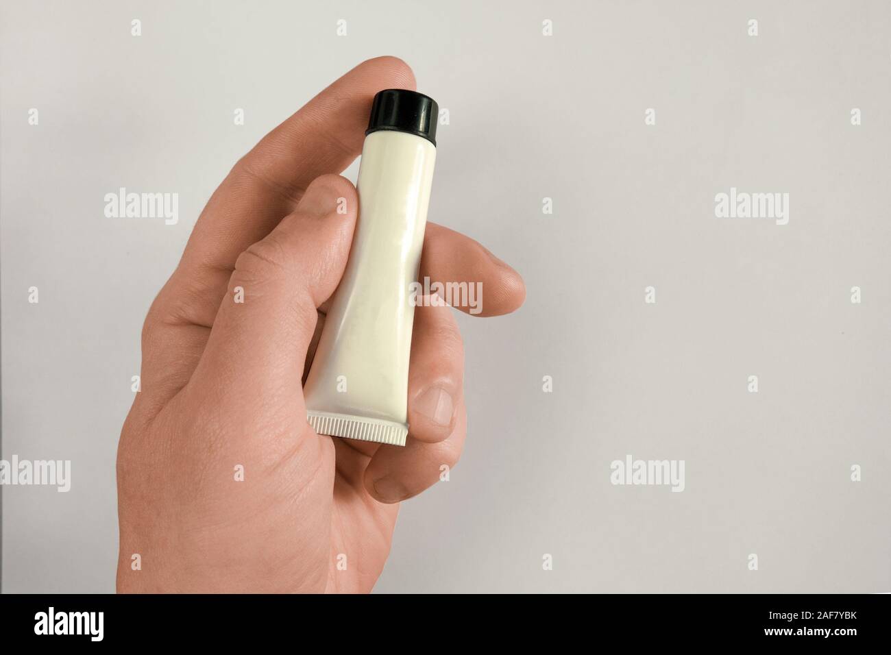 Mann Hand hält Rohr mit Creme, Gel oder Einfügen. Mock-up auf hellen Hintergrund mit Schatten und Kopieren. Im mittleren Alter Mann Body Care Konzept closeup Bild Stockfoto