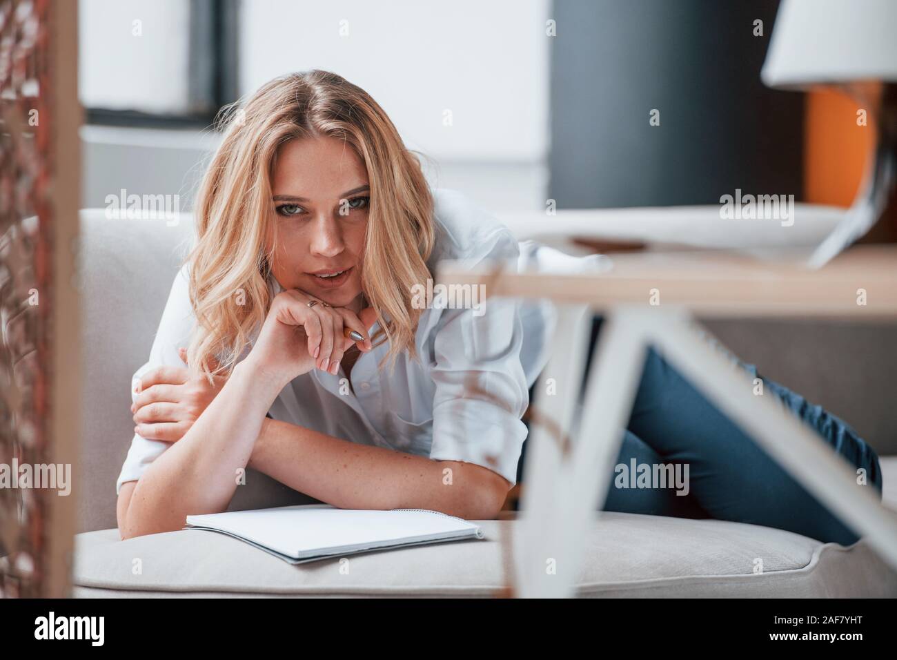 Liegend auf dem Sofa. Geschäftsfrau mit Lockigen, blonden Haaren sitzen im Zimmer gegen Fenster Stockfoto