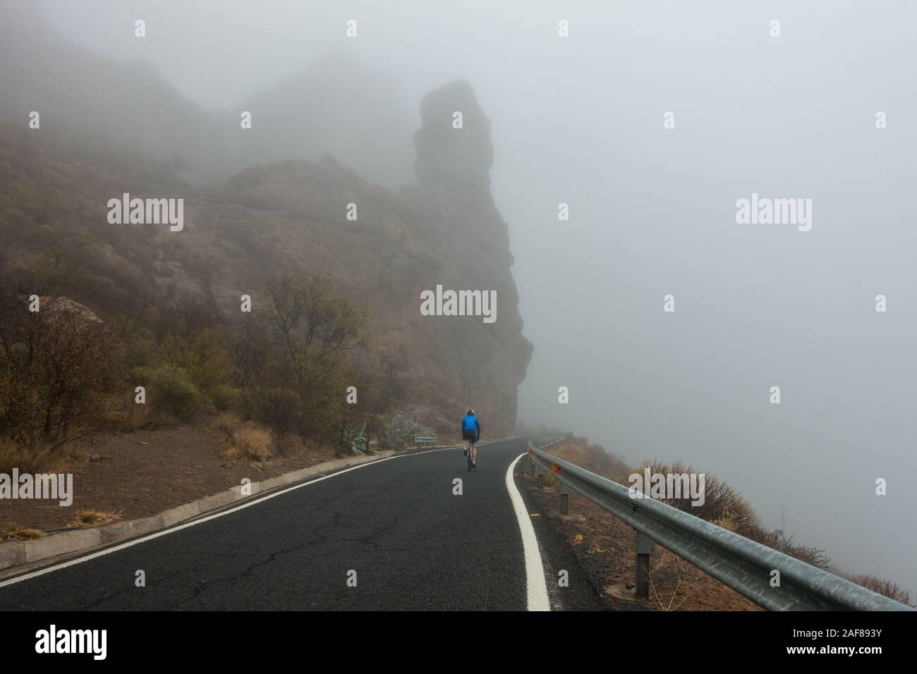 Person auf der Straße Fahrrad Radfahren bei schlechtem Wetter in den Bergen von Gran Canaria, Spanien (GC-60 in der Nähe von Ayacata) Stockfoto