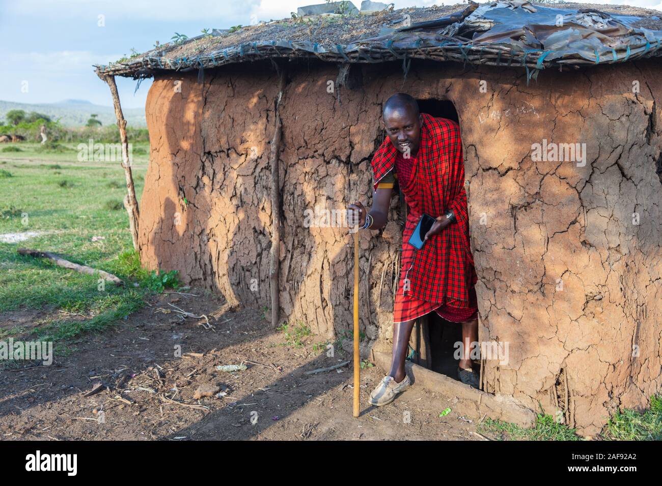 Tansania. Masai Mann verlassen sein Haus im Dorf Ololosokwan, nördliche Serengeti. Stockfoto