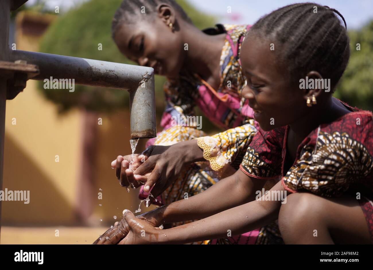 Erstaunliche afrikanische Schulkinder Mädchen, die reines Wasser von der Pumpe trinken - Weltwassertag Stockfoto