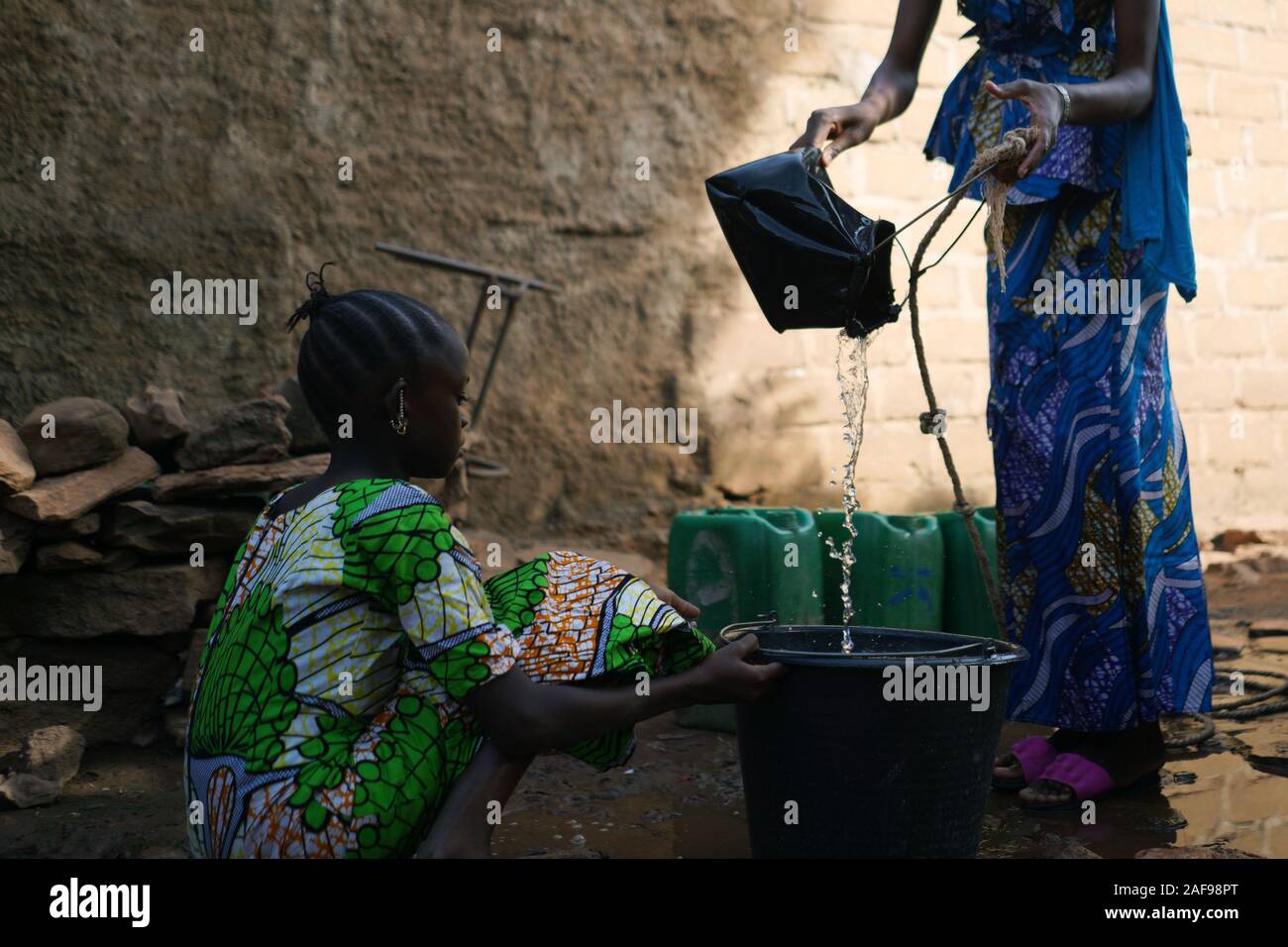 Nahaufnahme von afrikanischen schwarzen Kinder gießen Wasser aus einem Brunnen in den Eimer Stockfoto