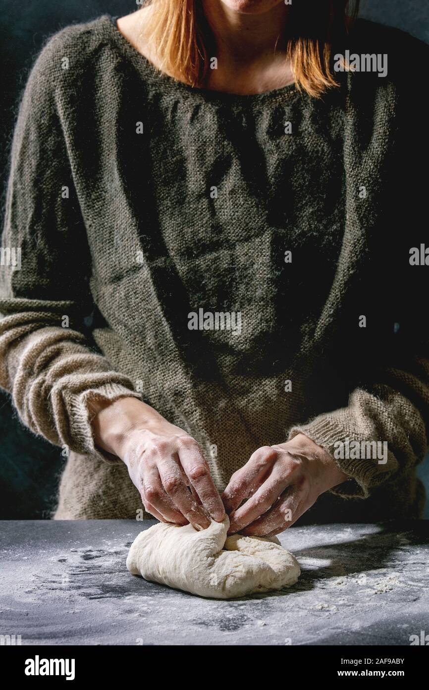 Prozess der Herstellung hausgemachte Brotteig. Weibliche Hände kneten den Teig auf dunklen Küche. Schwarzer Tisch mit Mehl. Home Brot backen. Foto Serie. Stockfoto