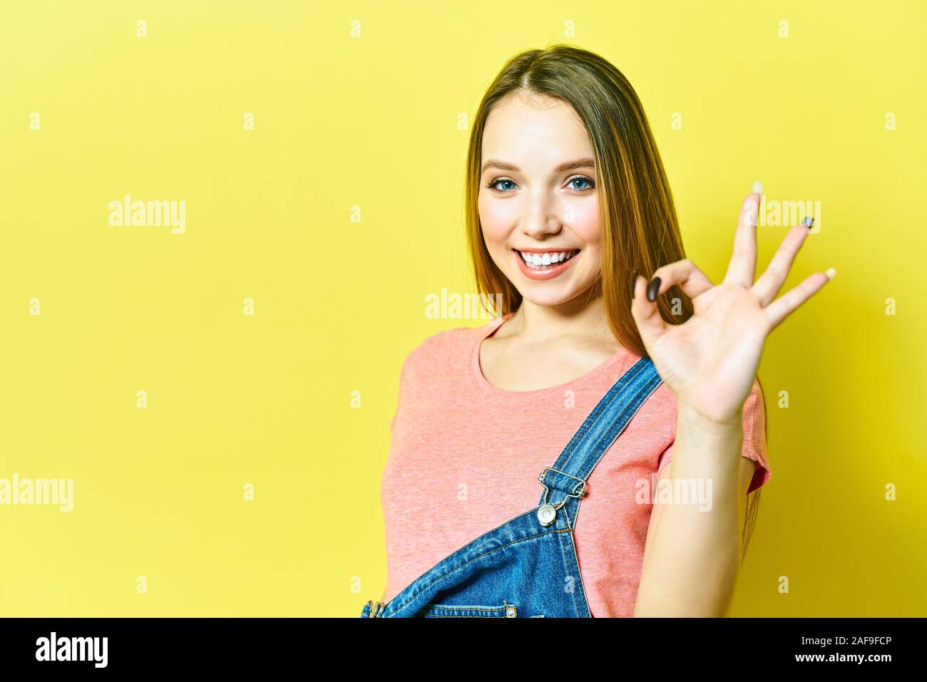 Lustige und fröhliche Mädchen zeigt okay unterzeichnen und zwinkert Kamera auf gelbem Hintergrund. Stockfoto