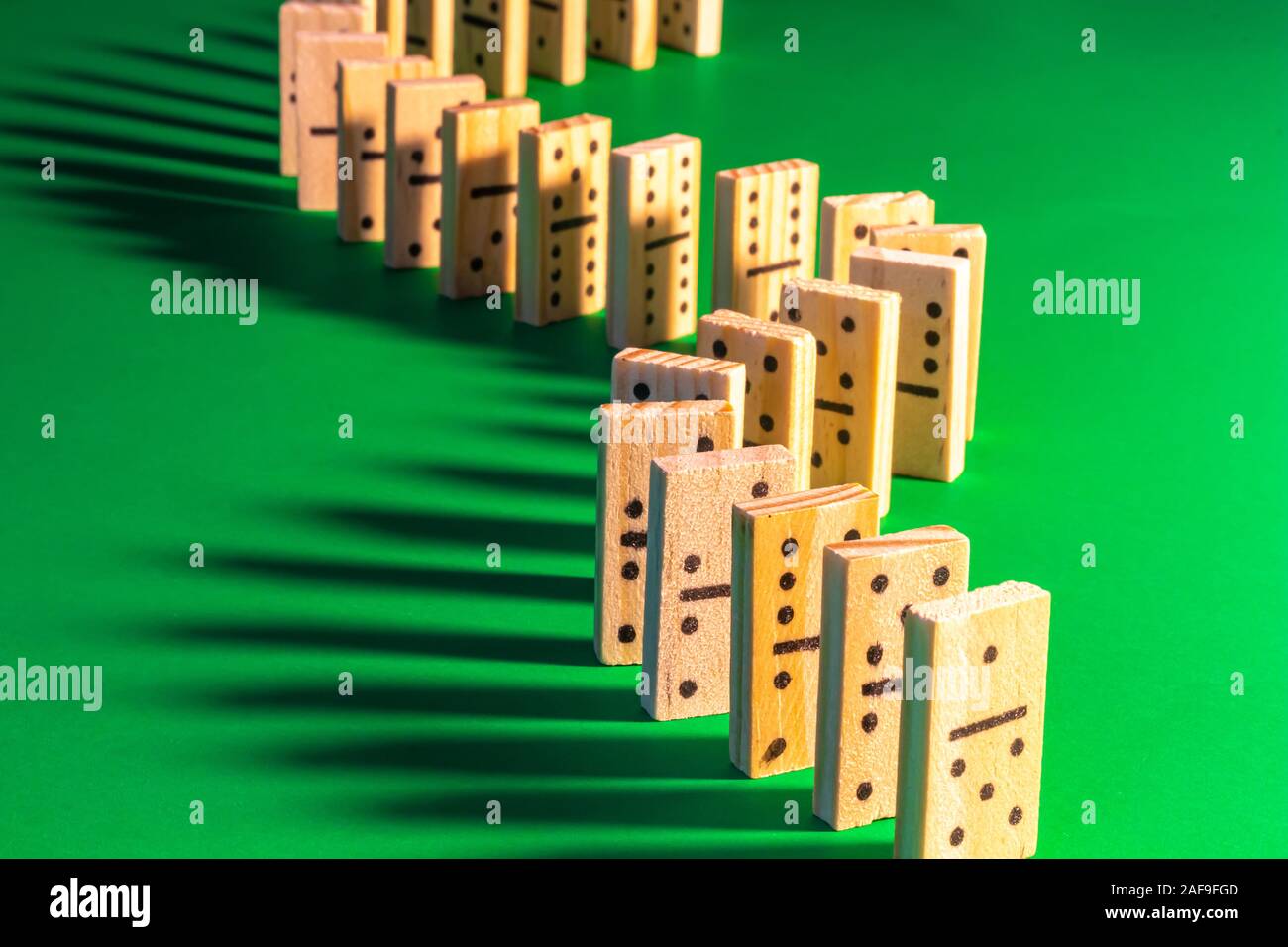 Eine geschwungene Linie von stehendem Holz- Domino auf Grün wird gesehen von Rechts beleuchtet, wodurch lange Schatten fallen auf der linken Seite. Die domino Show ist re Stockfoto