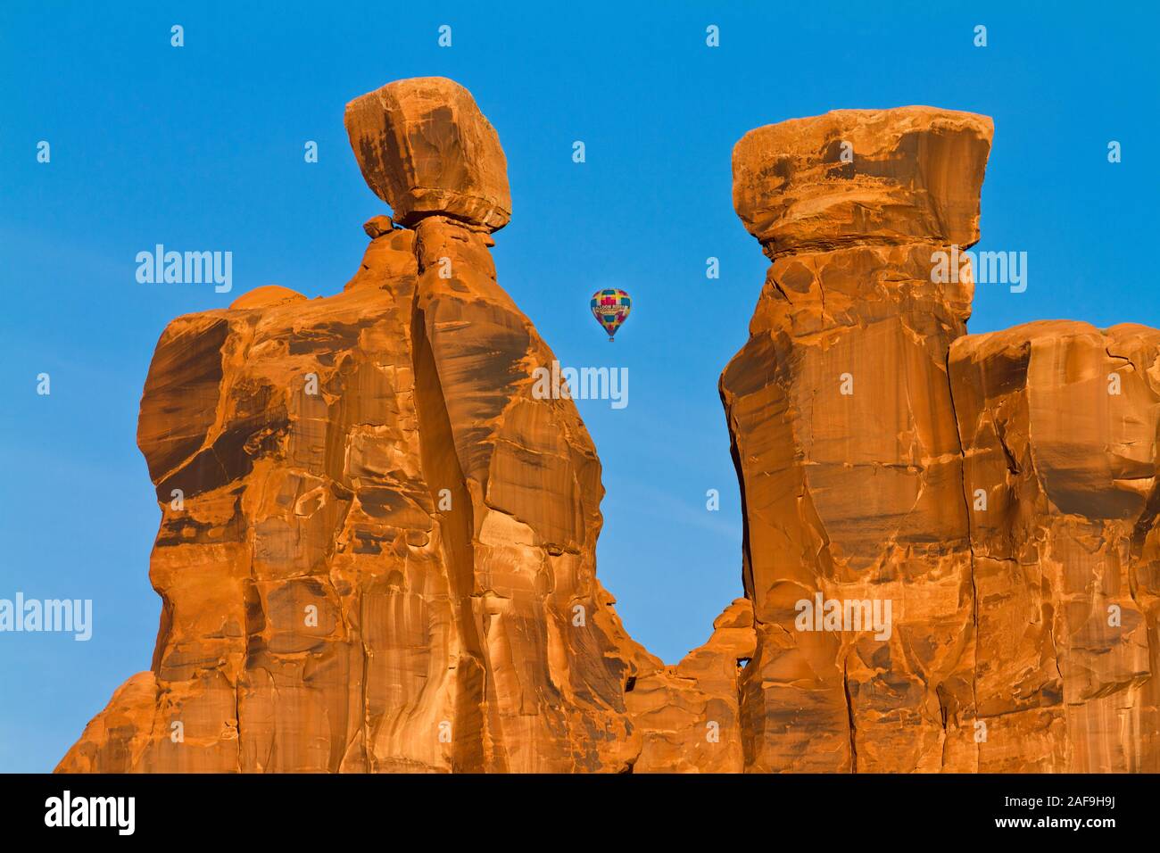 Ein Heißluftballon über der Arches National Park in der Nähe von Moab, Utah fliegen. Im Vordergrund steht die Felsformation bekannt als die Drei Klatschbasen. Stockfoto