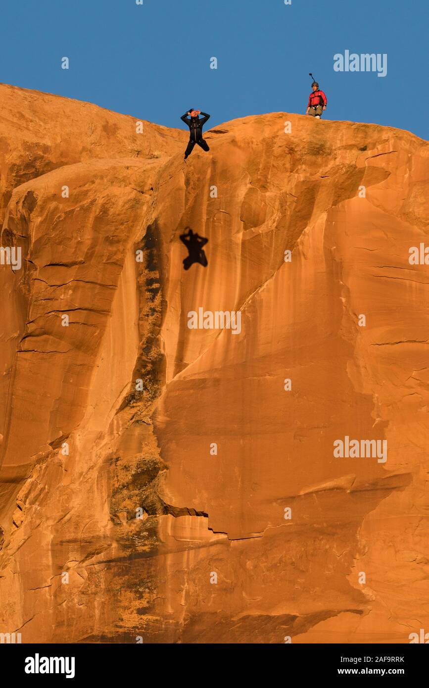 Ein BASE jumper Sprünge von der Spitze des 400-Fuß vertikale Teilfläche der Tombstone in der Kane Springs Canyon in der Nähe von Moab, Utah. Hinweis seinen Schatten auf die Klippe. Stockfoto