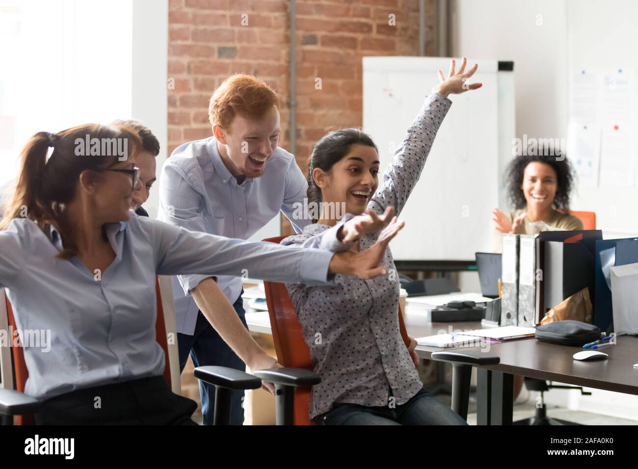 Diverse Arbeiter feiern große Nachrichten Reiten auf Bürostühle Stockfoto