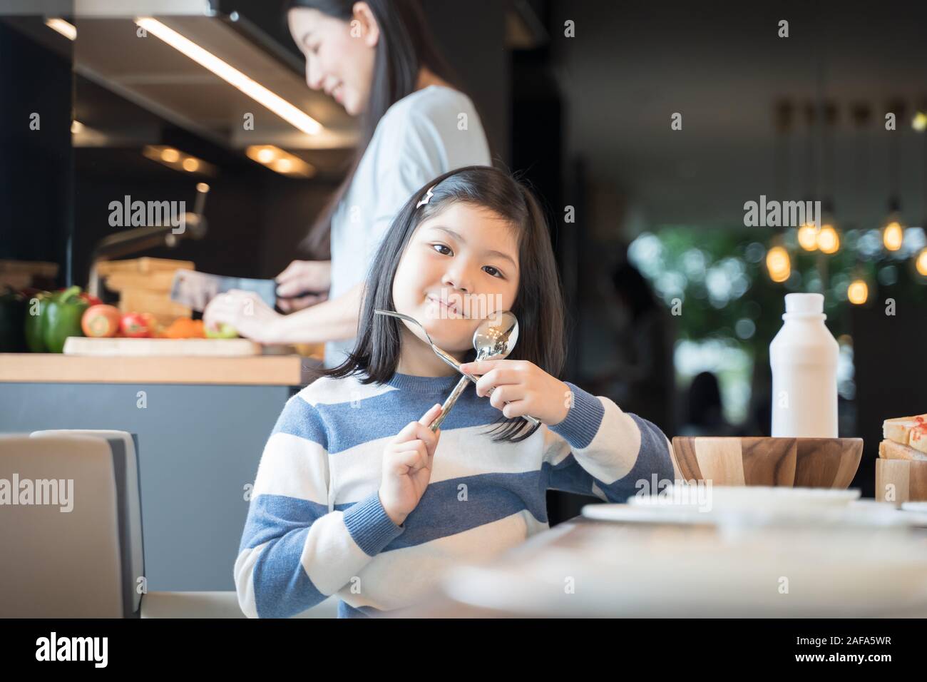 Mutter und Tochter essen Getreide mit Milch beim Frühstück in der Küche. Stockfoto