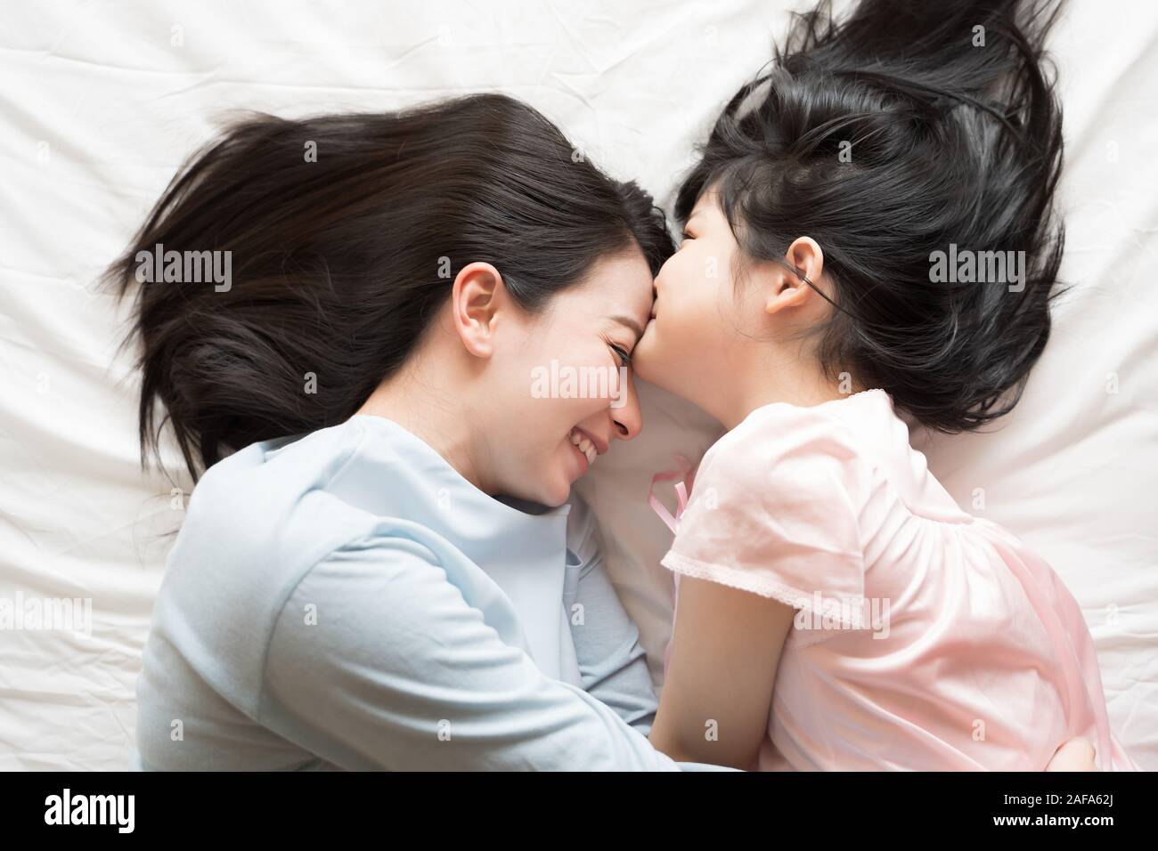 Tochter küsse Stirn der Mutter. Und umarmen im Schlafzimmer. Gerne asiatische Familie Stockfoto