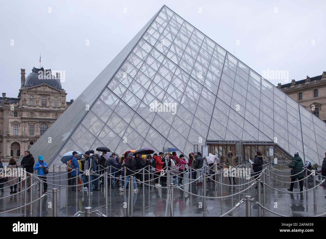 Am frühen Morgen Warteschlangen von Menschen, die in der Pyramide Eingang zum Louvre Museum in Paris, auf einer nassen Winter Tag Stockfoto