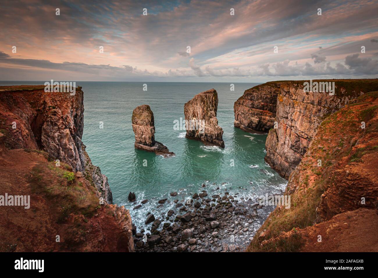 Stack rocks fotografiert bei Sonnenaufgang auf dramatische Küste von Pembrokeshire, South Wales, UK. Moody, farbenfrohen Himmel über der Bucht mit türkisfarbenem Wasser. Küste. Stockfoto