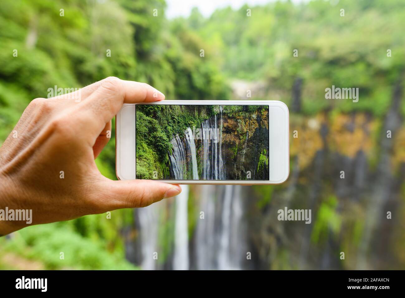Ein Tourist ist das Aufnehmen von Fotos mit einem Smartphone zu den schönen Tumpak Sewu Wasserfälle. Tumpak Sewu Wasserfälle sind eine touristische Attraktion im East Java. Stockfoto