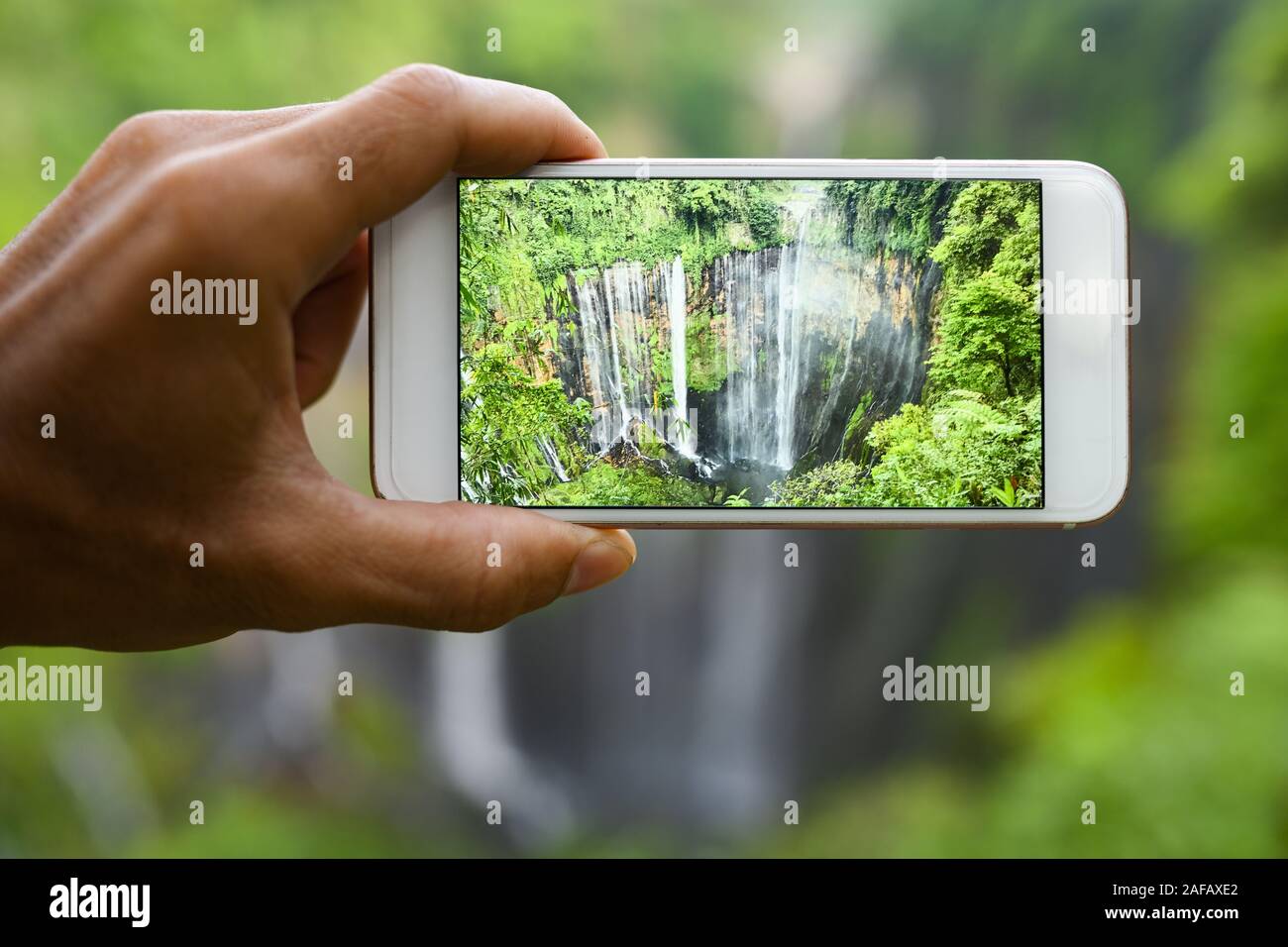 Ein Tourist ist das Aufnehmen von Fotos mit einem Smartphone zu den schönen Tumpak Sewu Wasserfälle. Tumpak Sewu Wasserfälle sind eine touristische Attraktion im East Java. Stockfoto