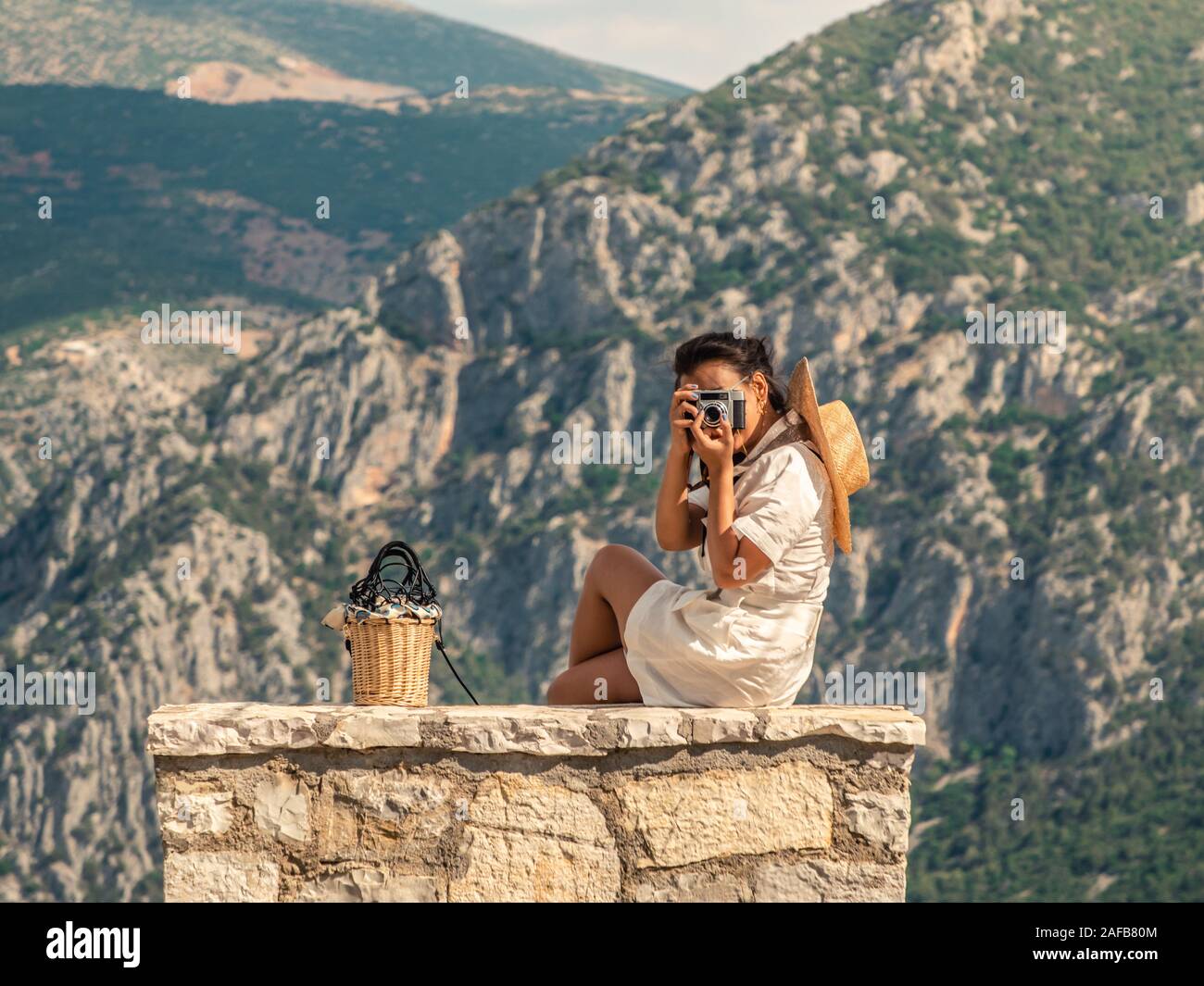 Junge Frau in Mode Kleid sitzt auf Stein becnch, die Bilder vor der Delfi Berglandschaft in Delphi, Griechenland Stockfoto