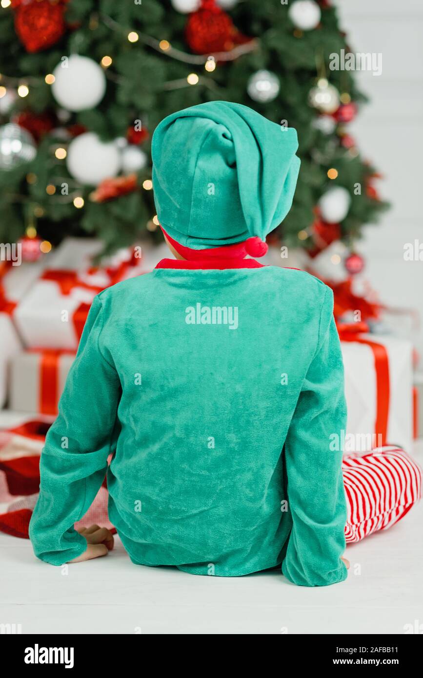 Junge öffnen Geschenke unter Weihnachten Baum auf Morgen. Kleinkind Junge sitzt auf dem Boden öffnen Geschenke. Kind unter dem Weihnachtsbaum mit Geschenkboxen. Deco Stockfoto