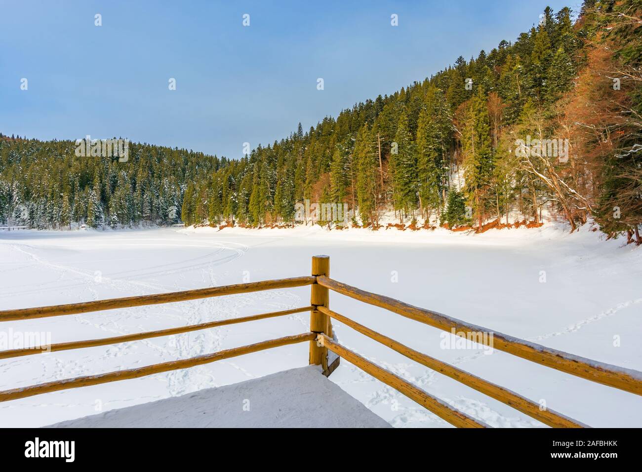 Zaun auf dem Holzsteg am See. Wunderbares sonniges Wetter im Winter. gefrorenen See synevyr mit Schnee bedeckt. Fichtenwald auf einem Ufer um. kleinen Baue Stockfoto