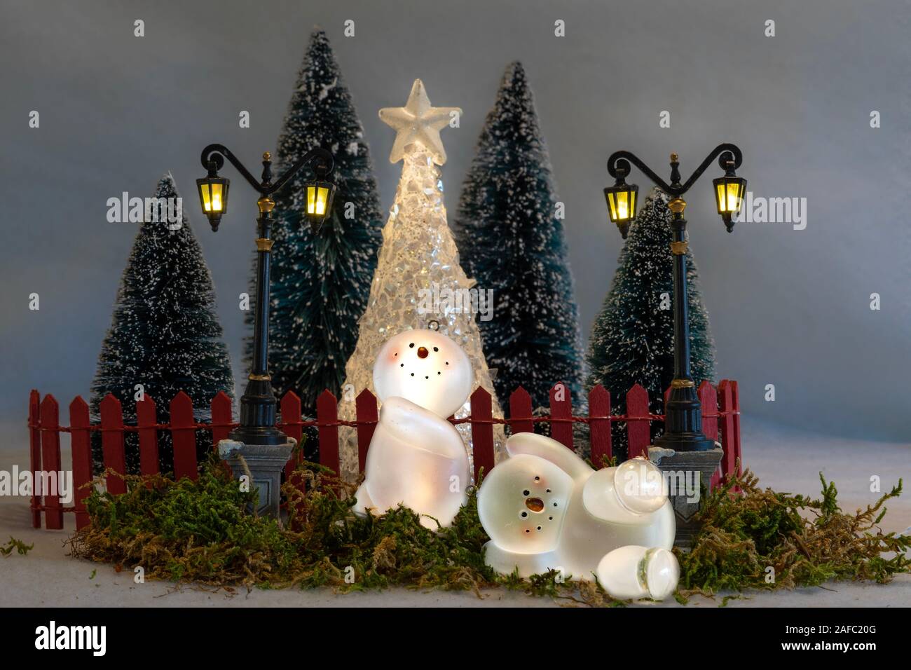 Weihnachtskarte, Spielzeug Schneemänner (Ornamente) Spaß vor einem umzäunten Garten mit Bäumen und Laternen. Stockfoto