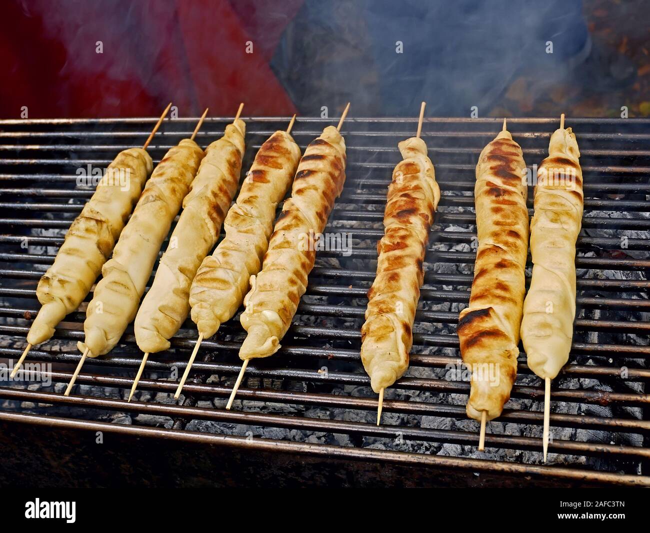 Fleischgericht in Teig um holzstäbchen aufgewickelt wird gegrillt am Bügeleisen Bars über einen Schwelbrand, close-up Stockfoto