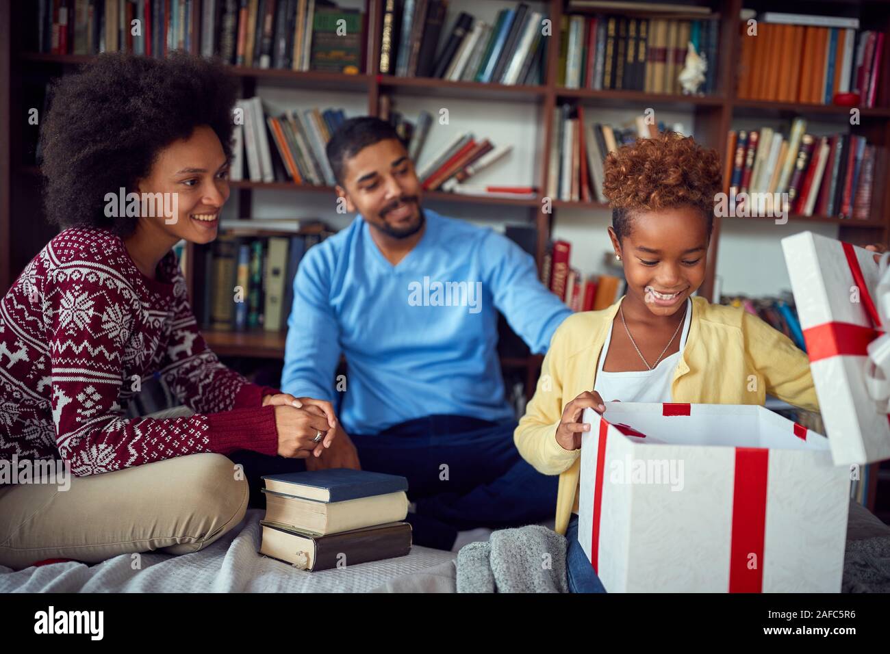 Fröhliches Kind öffnet sich ein Geschenk Weihnachten am Morgen mit lachenden Eltern. Stockfoto