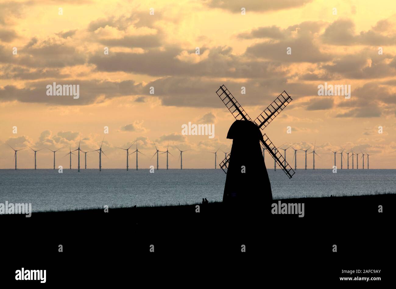 Blick auf die Rottingdean Windmühle, East Sussex, mit dem Offshore-Windpark Rampion in der Ferne, kurz vor Sonnenuntergang. Alte und neue Formen der Windenergie. Stockfoto