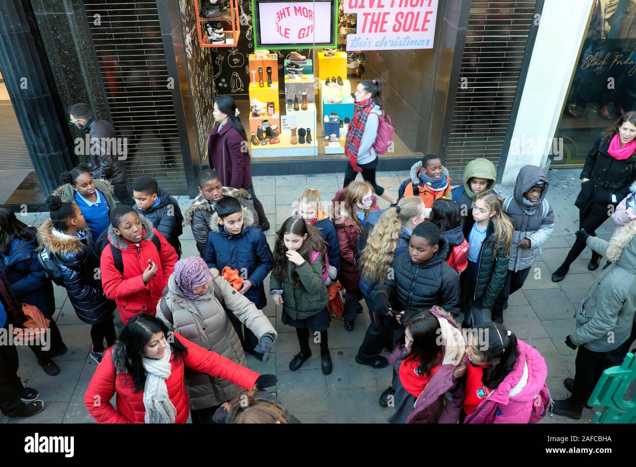 Gruppe von britischen Schulkindern und Lehrer warten auf einen Bus auf einem Einzelhandelsbesuch Städtetrip zur Oxford Street in London England Großbritannien KATHY DEWITT Stockfoto