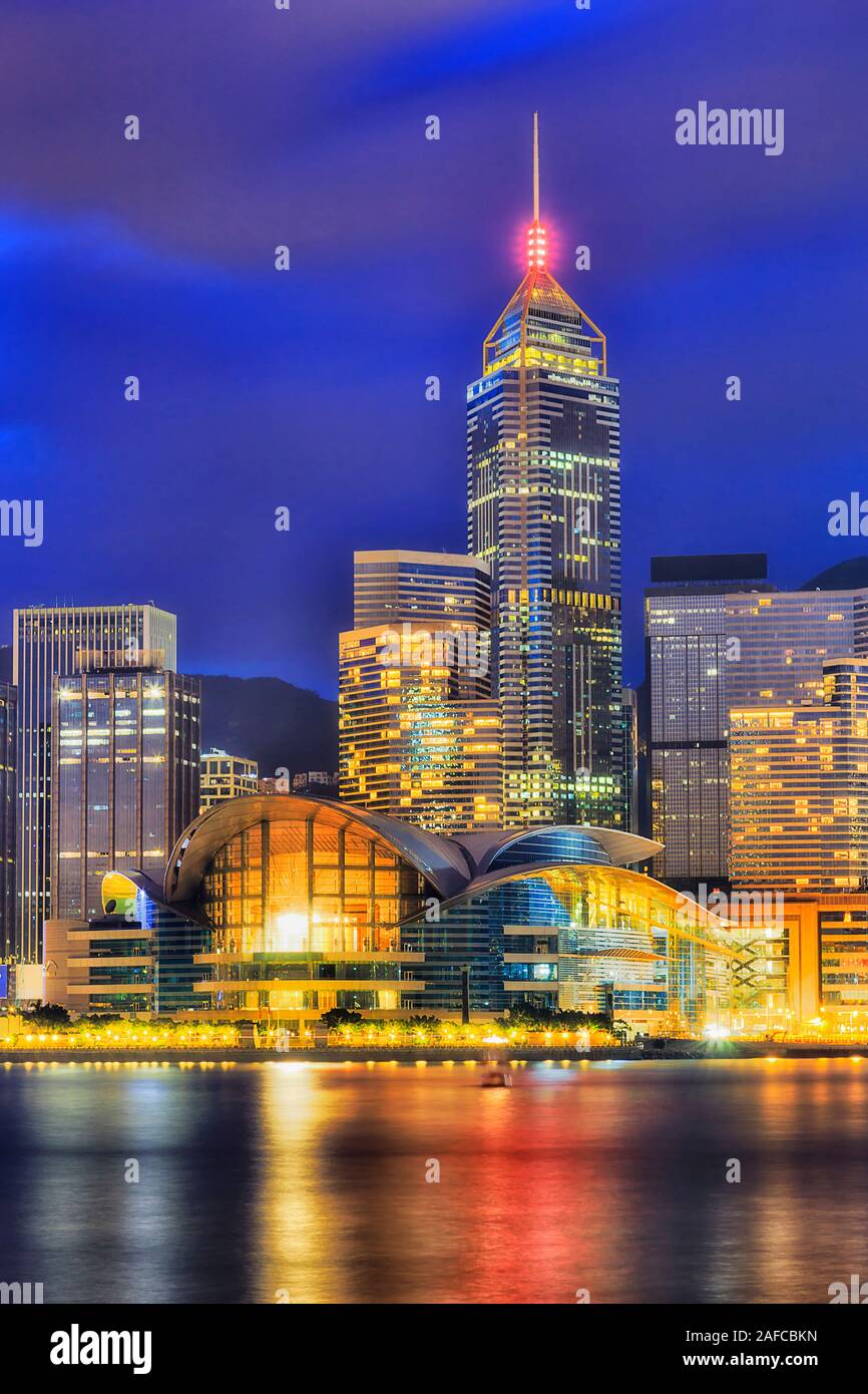 Helle Beleuchtung der modernen städtischen Gebäude auf Hong Kong Waterfront - Ufer des Victoria Harbour bei Sonnenaufgang gegen dark blue sky - vertikale Bild w Stockfoto