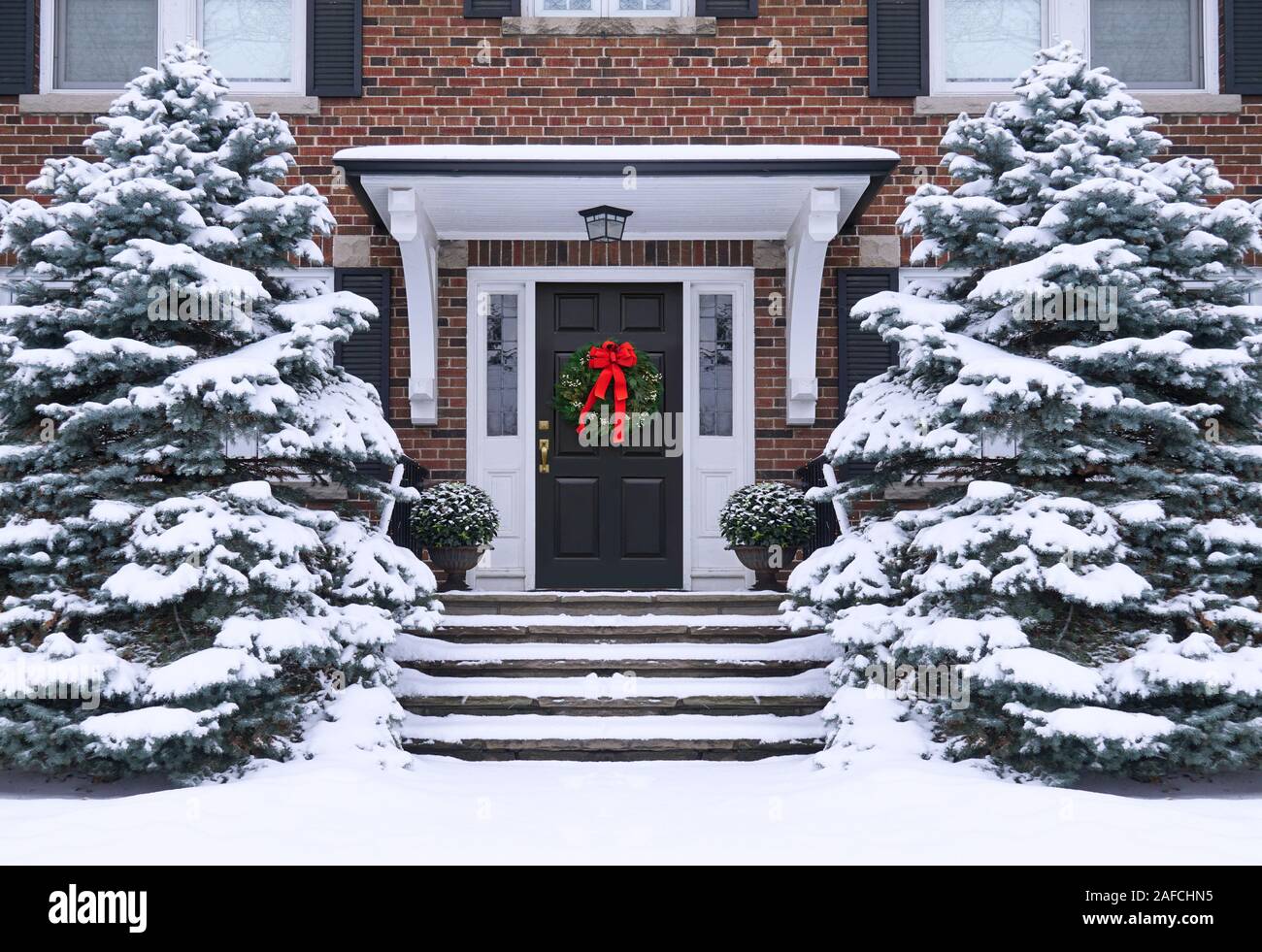 Vordere Tür des Hauses mit Weihnachten Kranz und schneebedeckten Pinien Stockfoto
