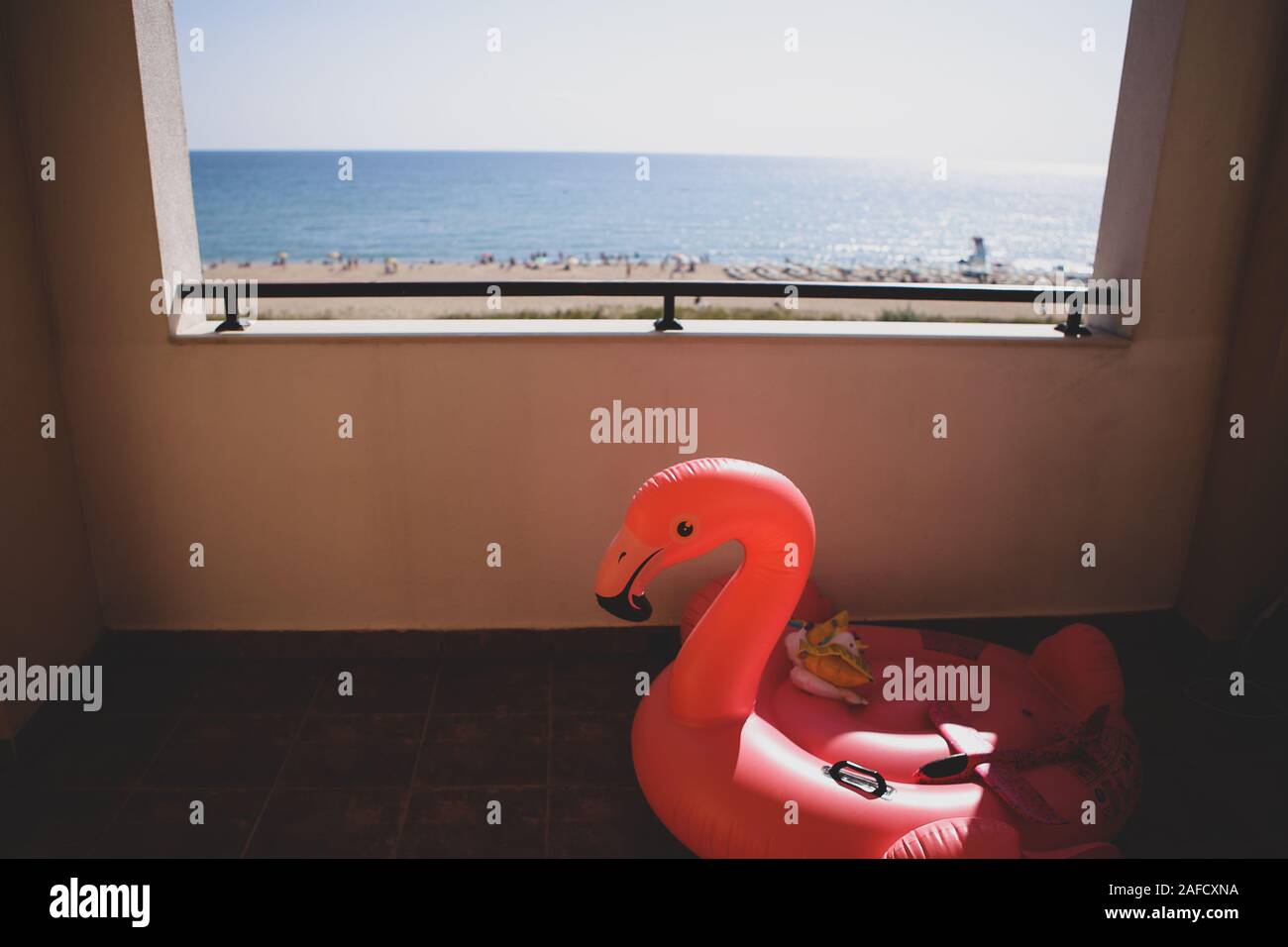 Flache Tiefenschärfe (selektive Fokus) Bild mit einem aufblasbaren rosa Flamingo auf der Terrasse des Hotels und der Strand und das Meer im Vordergrund. Stockfoto