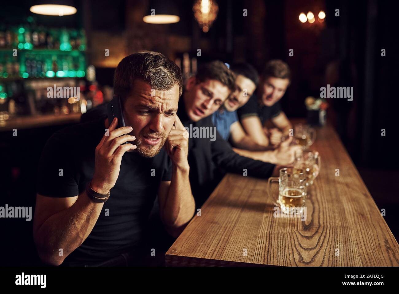 Man spricht von dem Telefon. Drei sport Fans in einer Bar beobachten Fußball. Mit einem Bier in der Hand Stockfoto