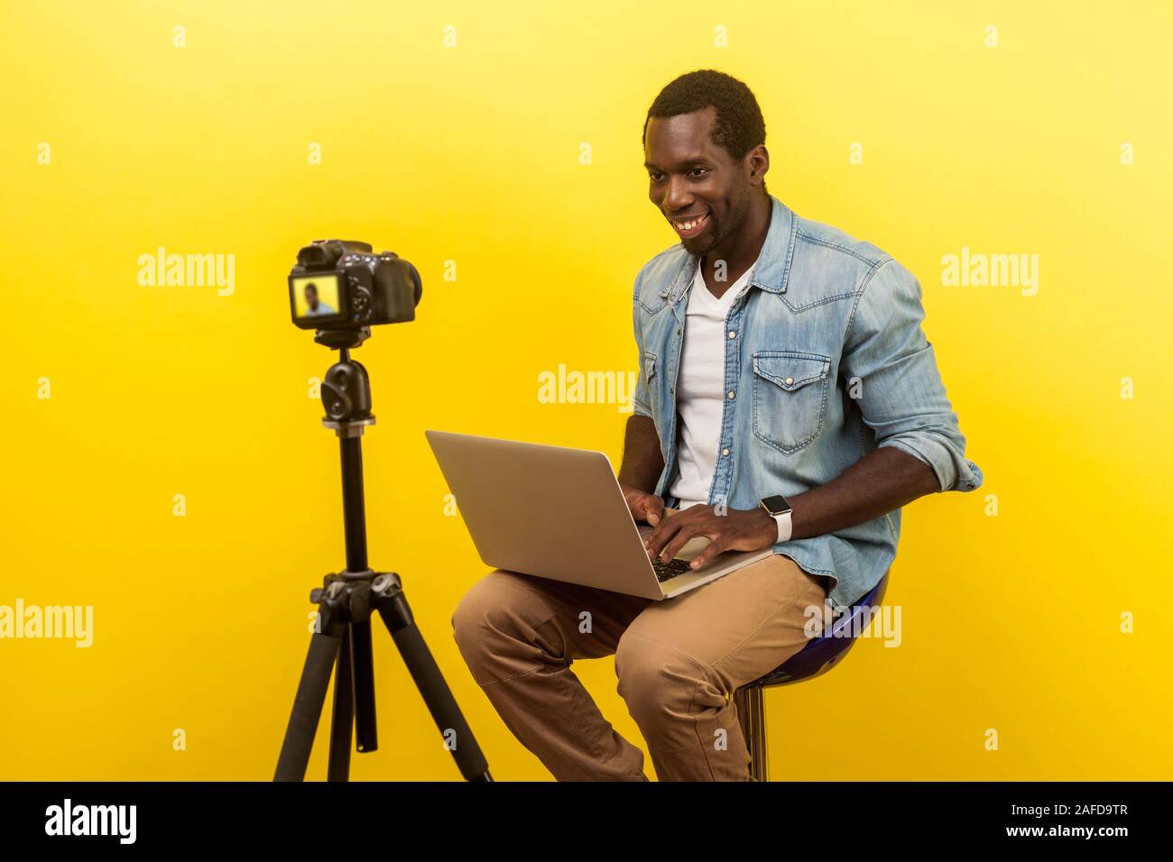 Portrait von professionellen fröhliche Fotograf in Jeanshemd compositing Foto Szene auf Laptop während der Aufnahme mit digitalen DSLR-Kamera. Stockfoto