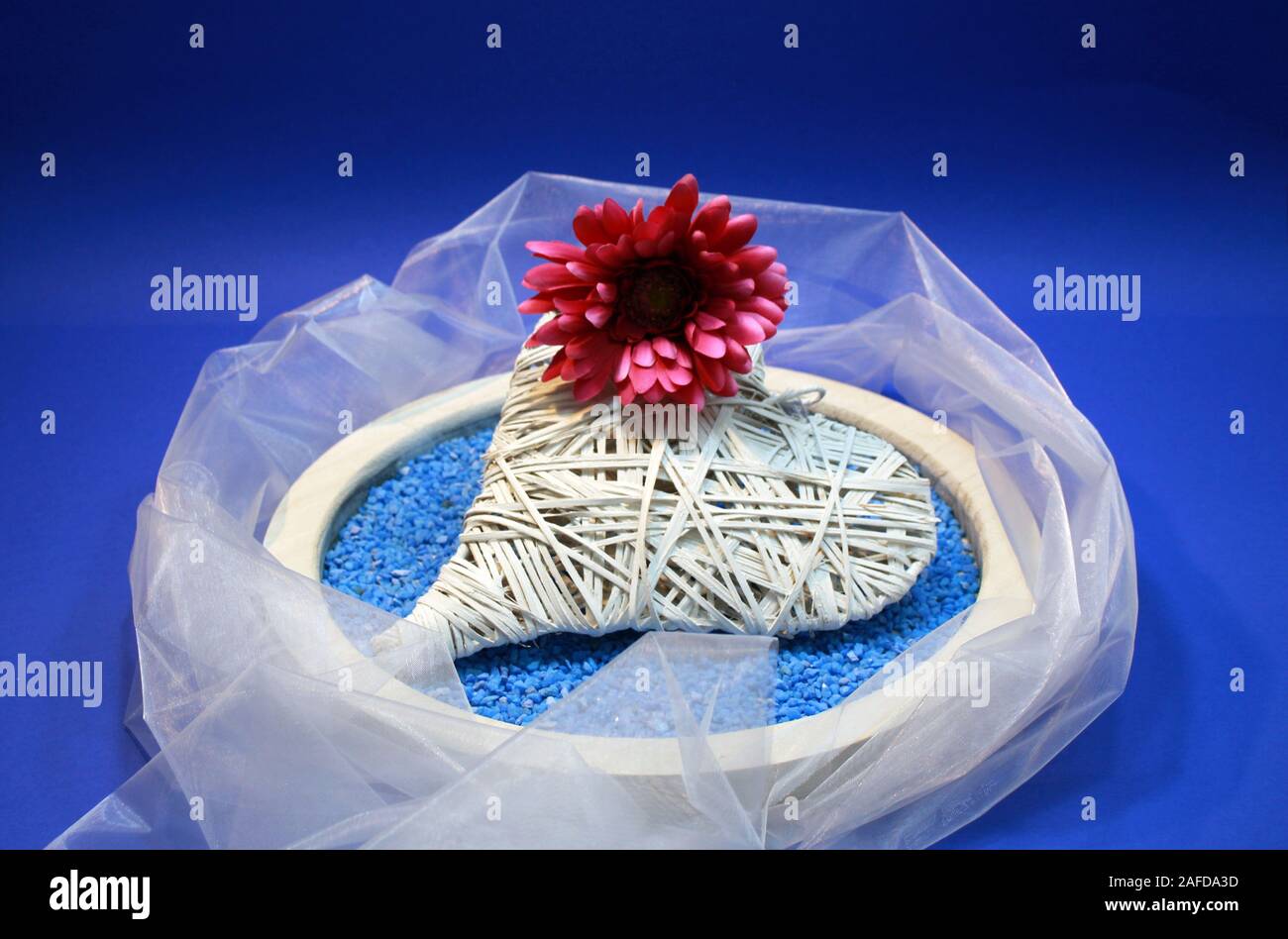 Herzen von Bast mit roter Baumwolle Chrysantheme auf Blau dekorative Steine in Houten Stockfoto